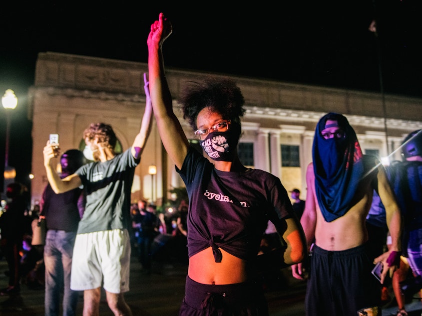 caption: Demonstrators raise their fist in the air, in front of law enforcement, on Aug. 25 in Kenosha, Wis. As the city declared a state of emergency curfew, a third night of civil unrest occurred after the shooting of Jacob Blake, 29, on Aug. 23.