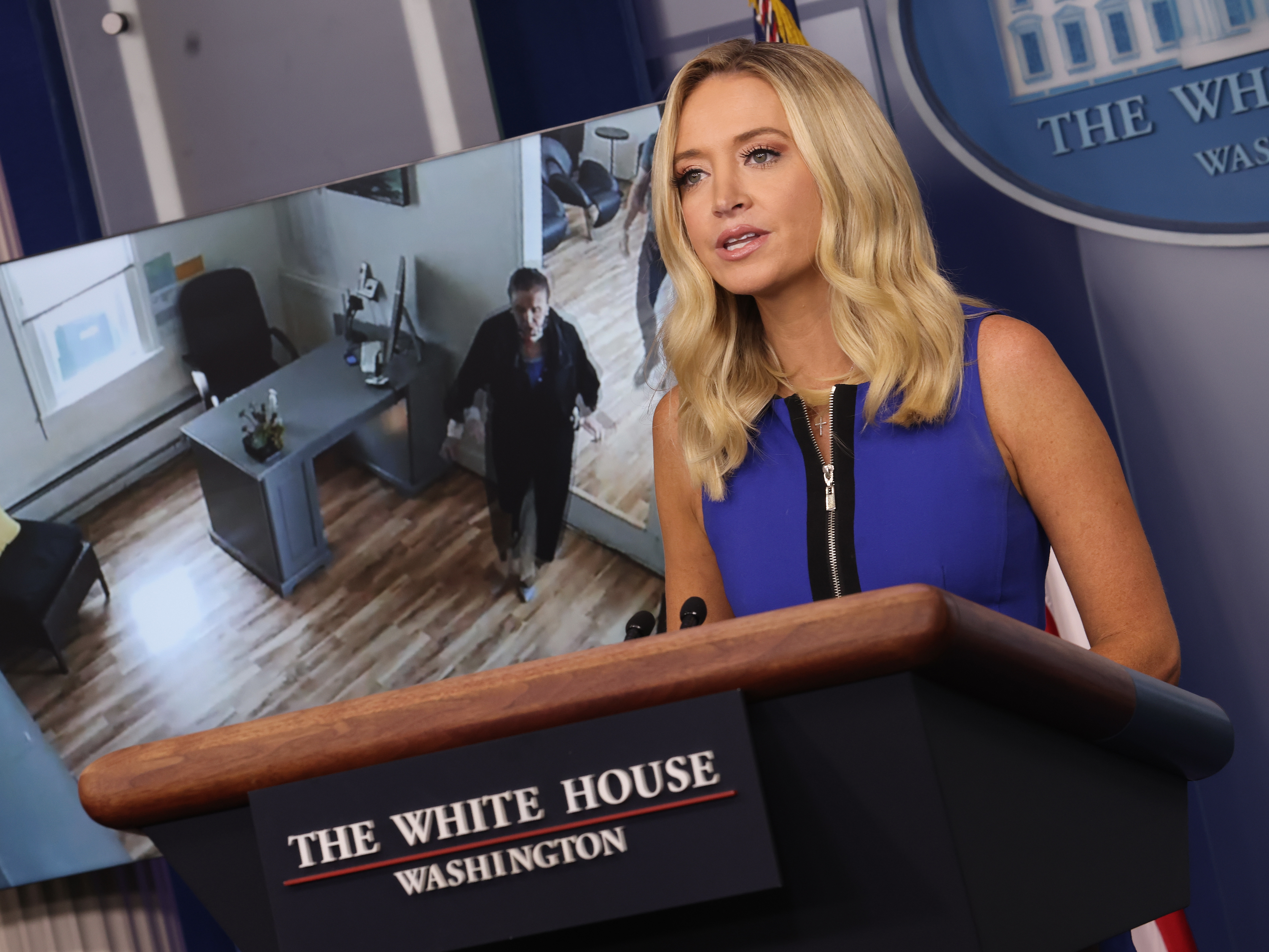 caption: White House press secretary Kayleigh McEnany holds a briefing Thursday as a video of House Speaker Nancy Pelosi entering a San Francisco hair salon plays in the background.