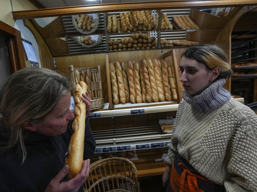 caption: Bakery owner Florence Poirier smells a baguette fresh from the oven Thursday as Mylene Poirier stands next to her at a bakery, in Versailles, west of Paris.