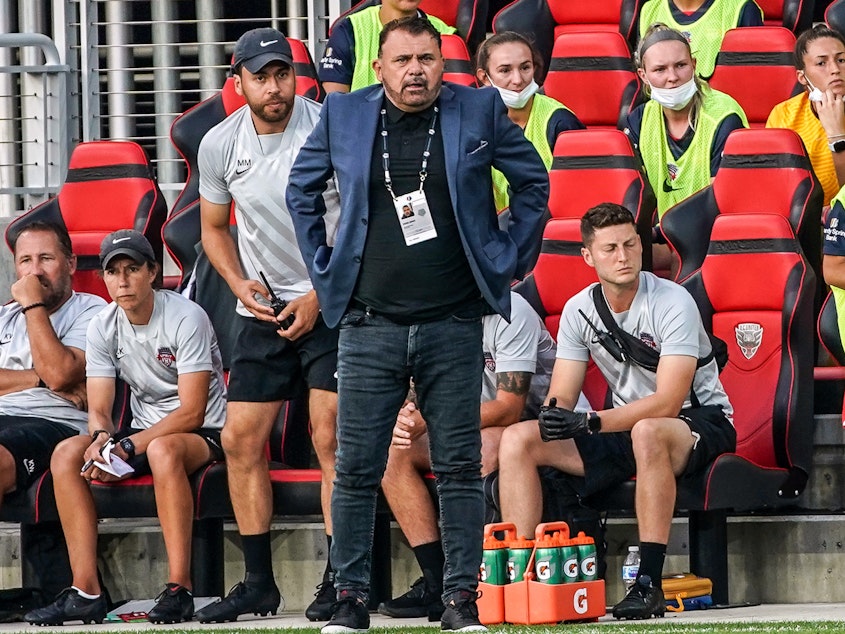 caption: Coach Richie Burke of the Washington Spirit watches the play during a game against the North Carolina Courage at Audi Field on July 10, 2021 in Washington, DC.