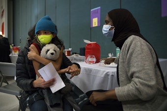 caption: Tejal Armes, 9, holds onto a stuffed panda bear shortly before registered nurse Iman Yunis with the Othello Station Pharmacy administers a Covid-19 vaccine on Wednesday, November 10, 2021, at Thurgood Marshall Elementary School in Seattle. 