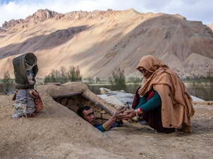 caption: Roqia Qasqari, right, who lives in Gero village in Afghanistan's Bamyan Province, inspects potatoes stored from a previous harvest. Snow was scarce over the winter, raising fears of a severe drought in 2021.