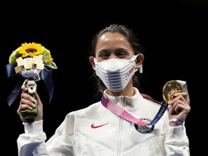 caption: Gold medalist Lee Kiefer of the United States shows her medal and victory bouquet during the medal ceremony for the women's individual foil final competition on Sunday at the Summer Olympics.