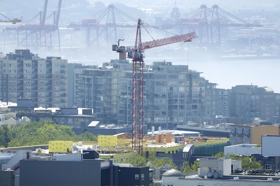 caption: A construction crane working on a building is shown with Port of Seattle cranes in the background on a foggy summer day, Monday, July 15, 2014, in Seattle. 