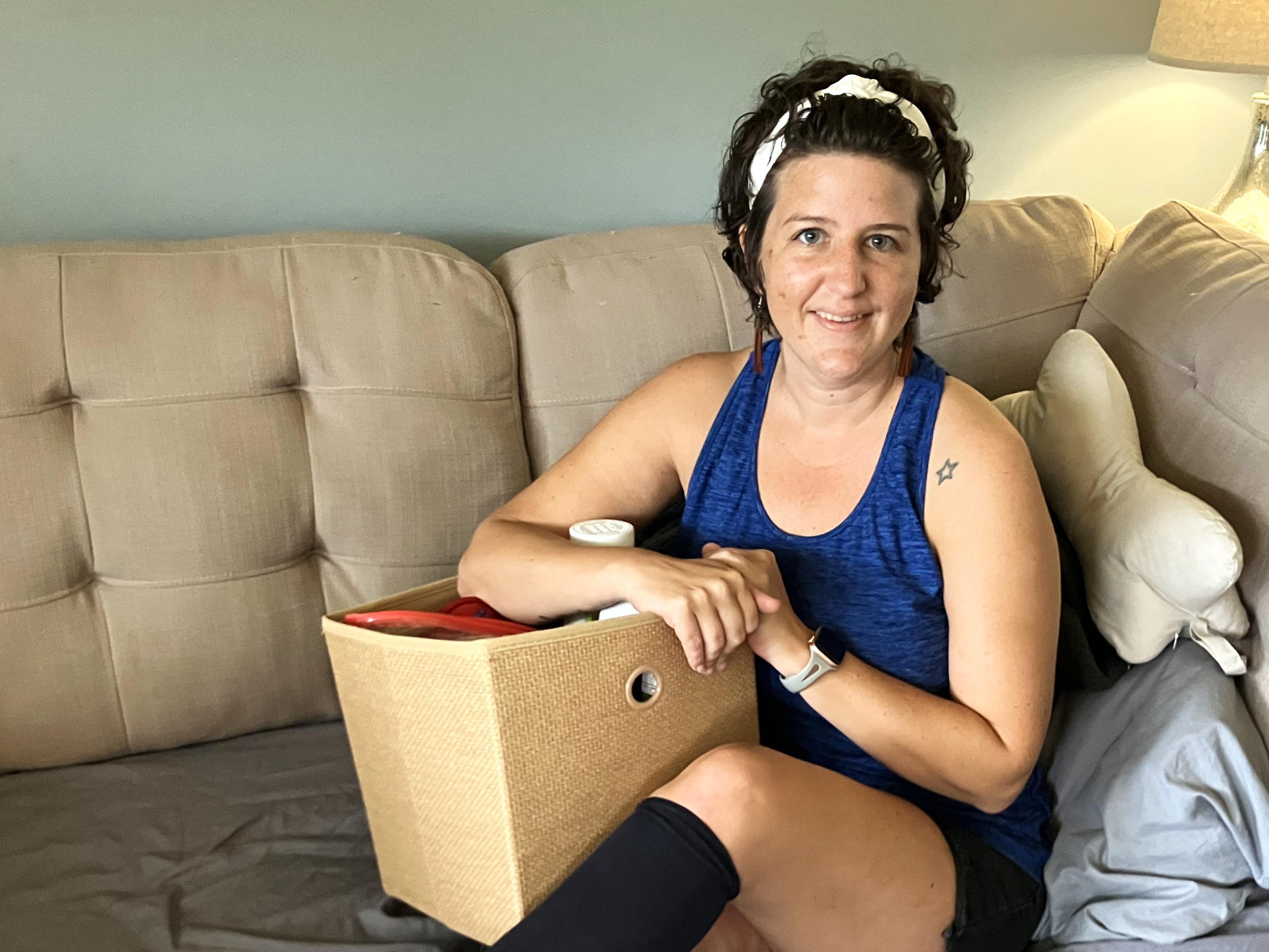 caption: Erica Hayes, 40, sits on her sofa with a box where she keeps the medical supplies she needs to manage her long COVID symptoms, which include chronic fatigue, irregular heart rate, low blood pressure, hives, migraines and internal tremors.