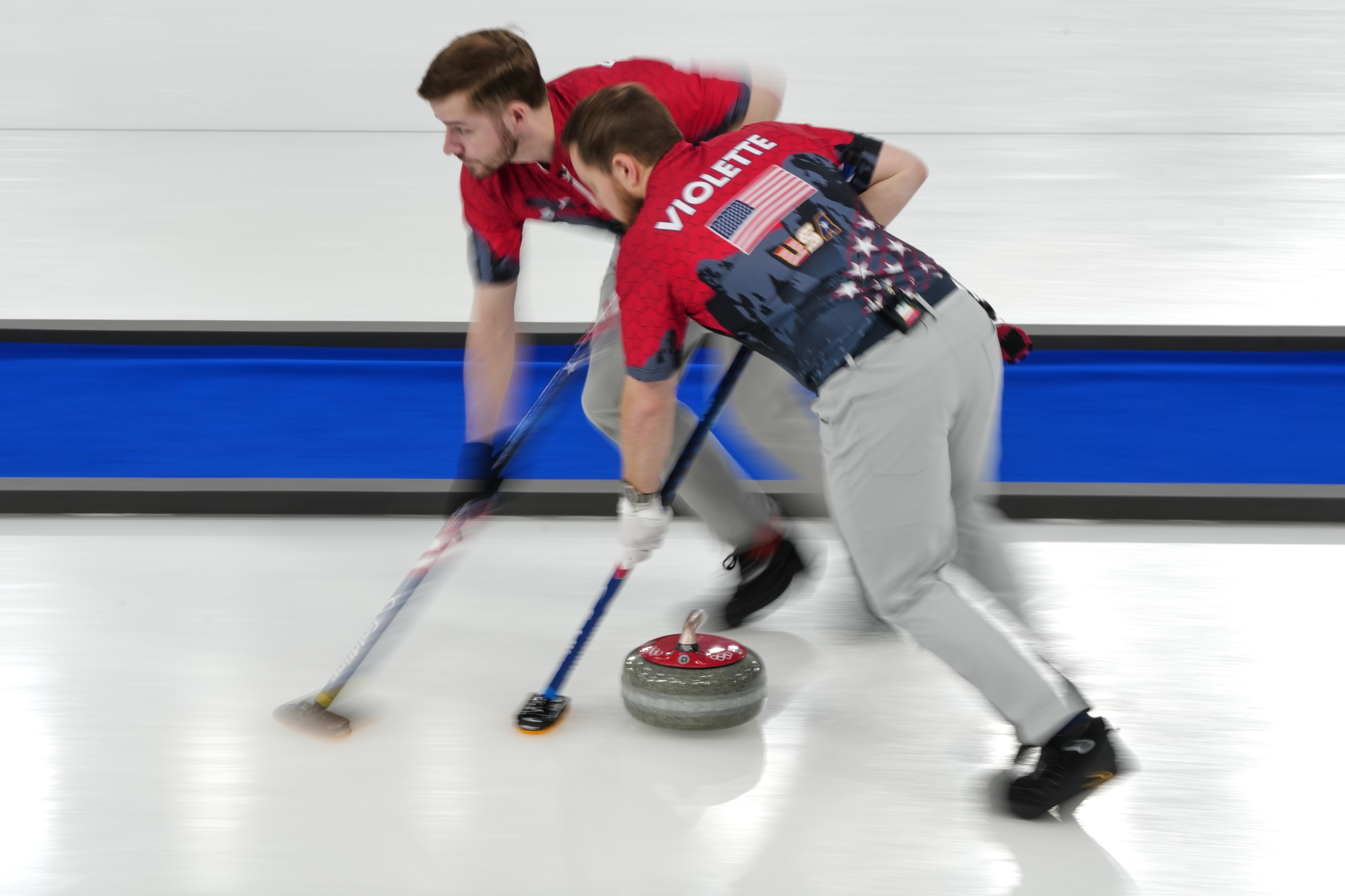 caption: United States' Luc Violette, and Ben Richardson in action during the men's curling round robin session against Britain, at the 2026 Winter Olympics, in Cortina d'Ampezzo, Italy, Wednesday, Feb. 18, 2026. 