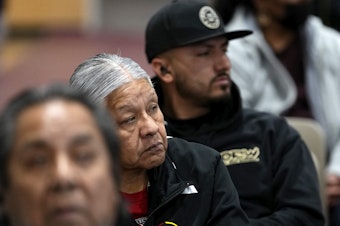 caption: Residents of Gila River Indian Community listen during a "Road to Healing" event at the Gila Crossing Community School in Laveen, Ariz. The year-long tour goes across the country to provide Indigenous survivors of the federal Indian boarding school system and their descendants an opportunity to share their experiences.