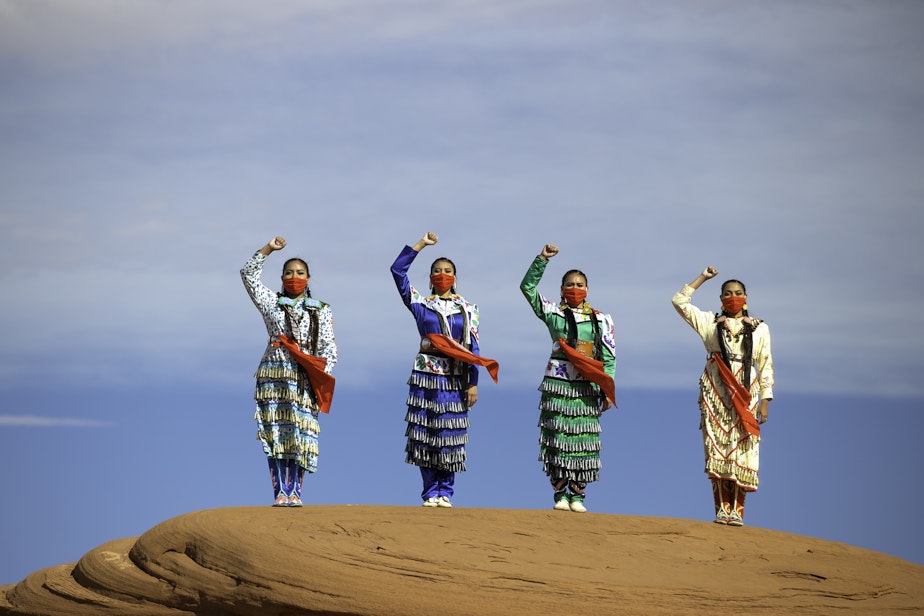 caption: Erin and Dion Tapahe and Sunni and JoAnni Begay pose with their fists raised on native land in Monument Valley.