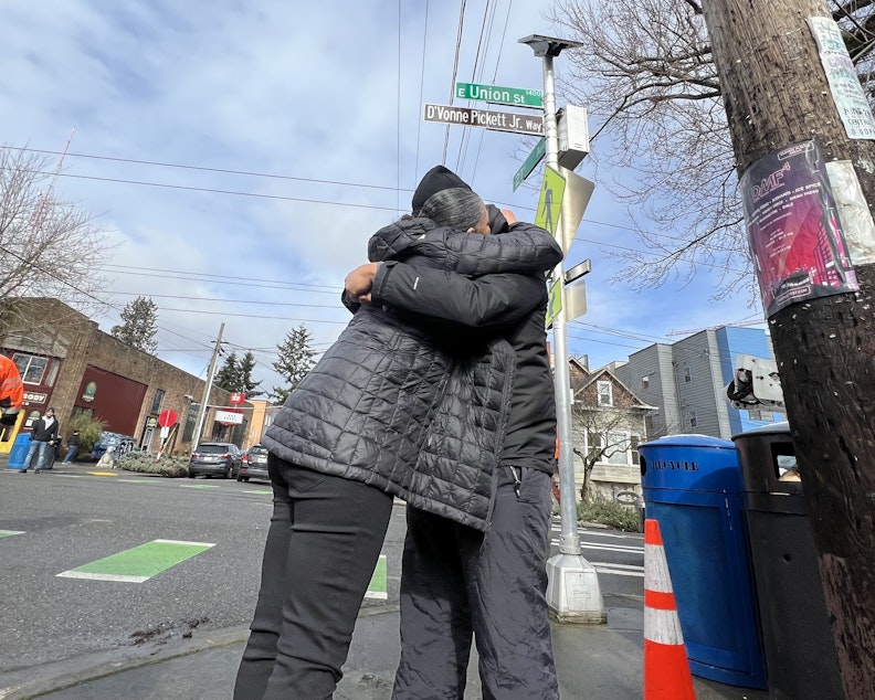caption: Nicky Chappell shares a hug under the new street sign honoring her son, D'Vonne Pickett Jr., who was fatally shot last October near his business in Seattle's Central District.
