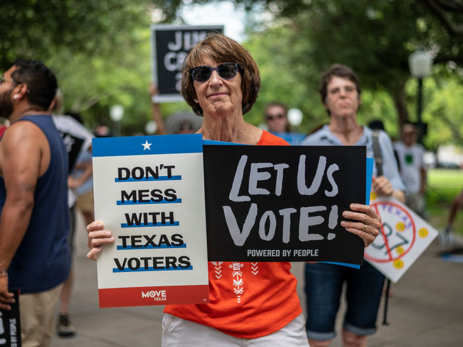 caption: A woman holds signs at a rally at the state Capitol on June 20 in Austin, Texas, to fight SB7, a controversial voting bill.