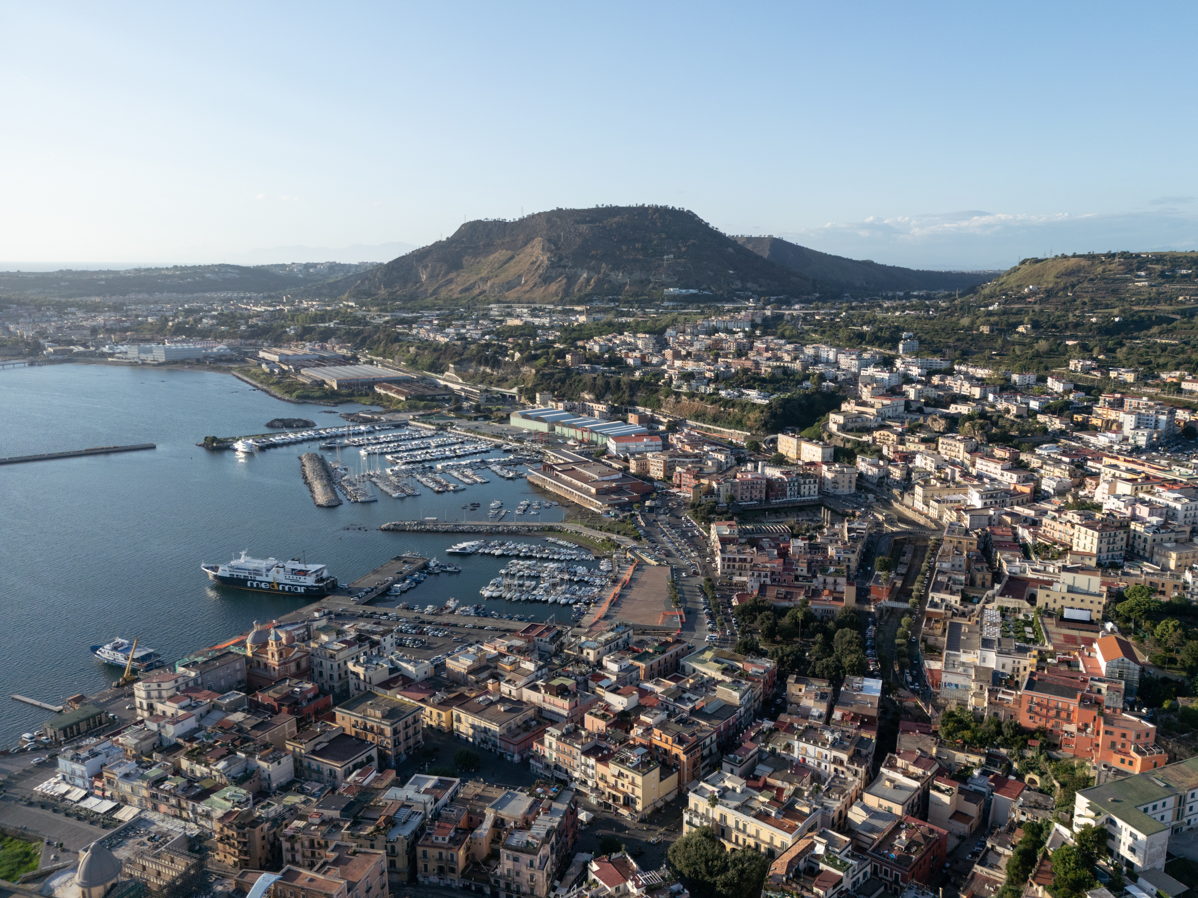 caption: Aerial view of the densely inhabited area of Pozzuoli, located within the Campi Flegrei volcanic area. Over half a million people live in this region, which is continuously monitored due to the ongoing volcanic activity.