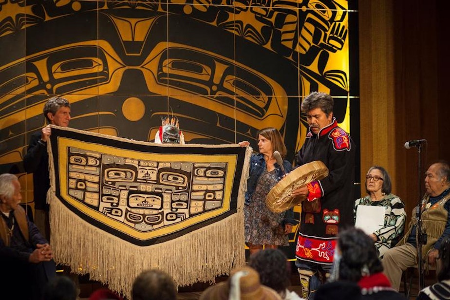 caption: Bruce and Gretchen Jacobsen hold the Chilkat robe they donated to the Sealaska Heritage Institute as Joe Zuboff, Deisheetaan, sings and drums and Brian Katzeek (behind robe) dances during the robe's homecoming ceremony Saturday, August 26, 2017.