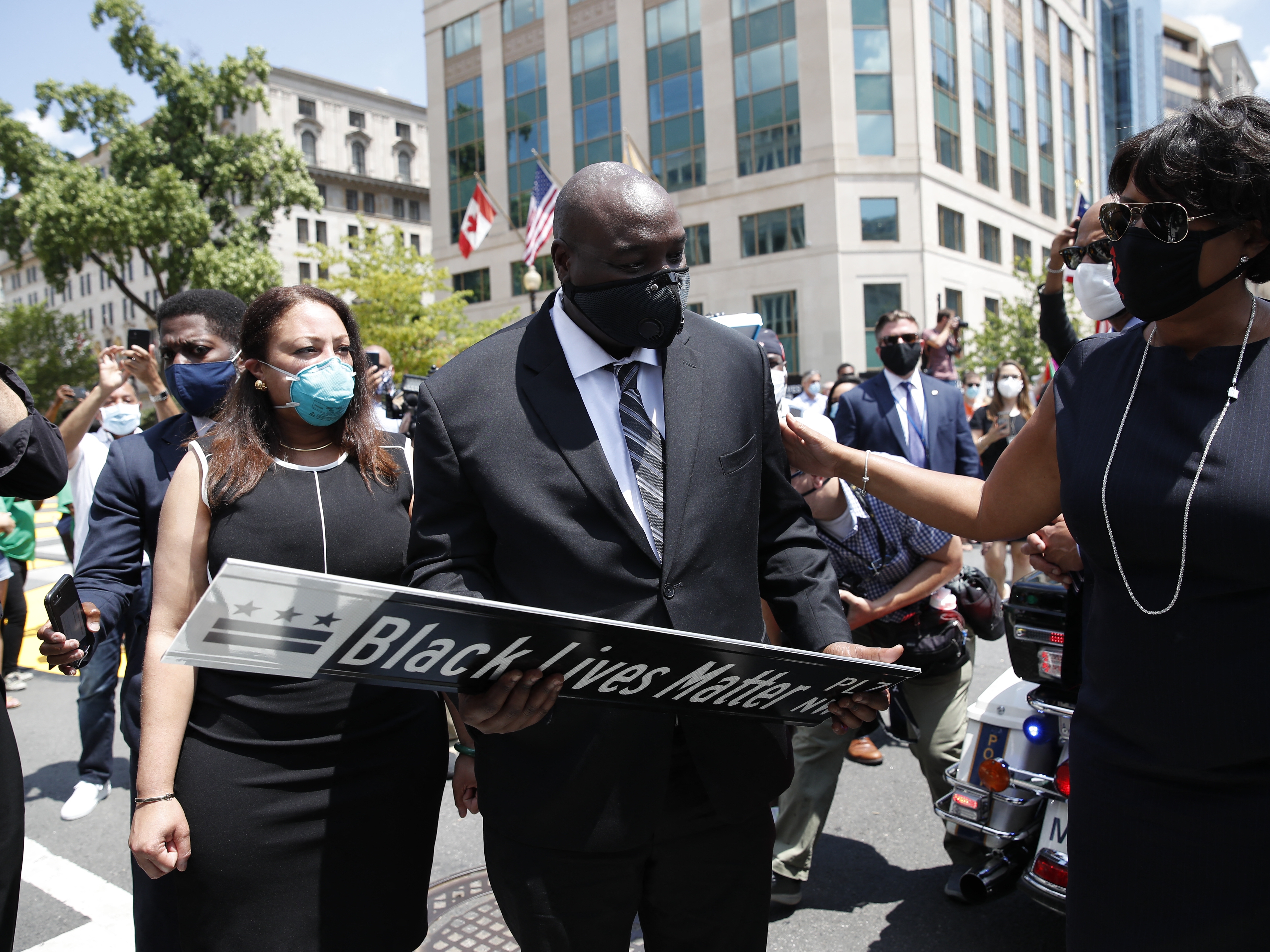 caption: District of Columbia Mayor Muriel Bowser (R) presents a Black Lives Matter Plaza street sign to a representative of the family as the hearse with the flag-draped casket of U.S. congressman and civil rights icon John Lewis drives on 16th Street, renamed Black Lives Matter Plaza, near the White House in Washington, DC July 27, 2020.