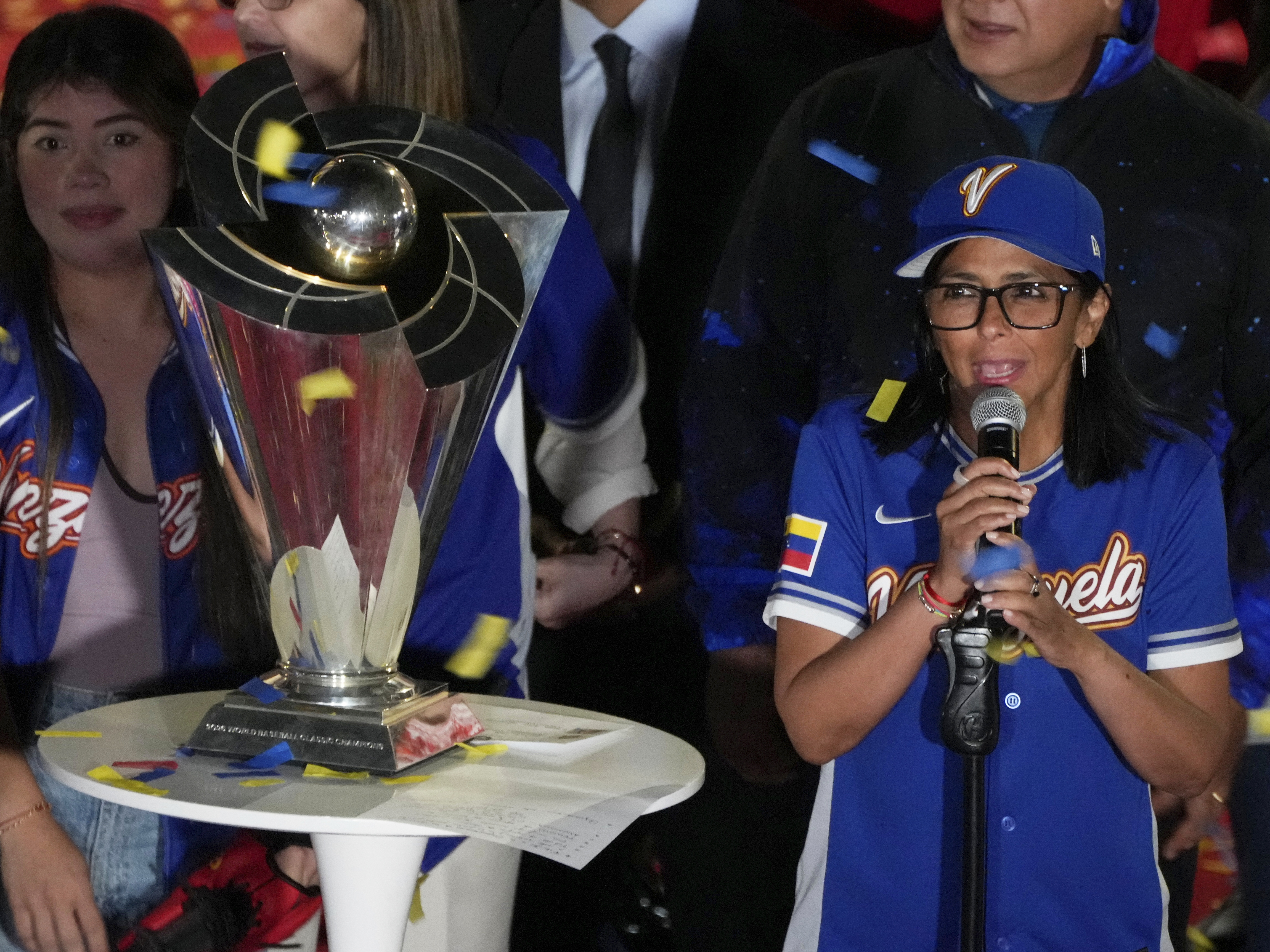 caption: Venezuela's acting President Delcy Rodriguez, right, speaks next to the World Baseball Classic trophy a day after her team's victory over the United States in the championship match, at Miraflores presidential palace in Caracas, Venezuela, Wednesday, March 18, 2026.