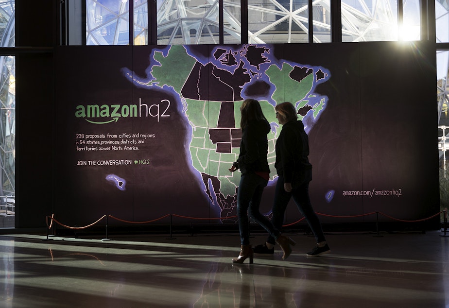 caption: Amazon employees walk in front of a map highlighting 238 cities that submitted bids for Amazon's second headquarters in the lobby of the Day 1 building on Tuesday, October 24, 2017, in Seattle. 