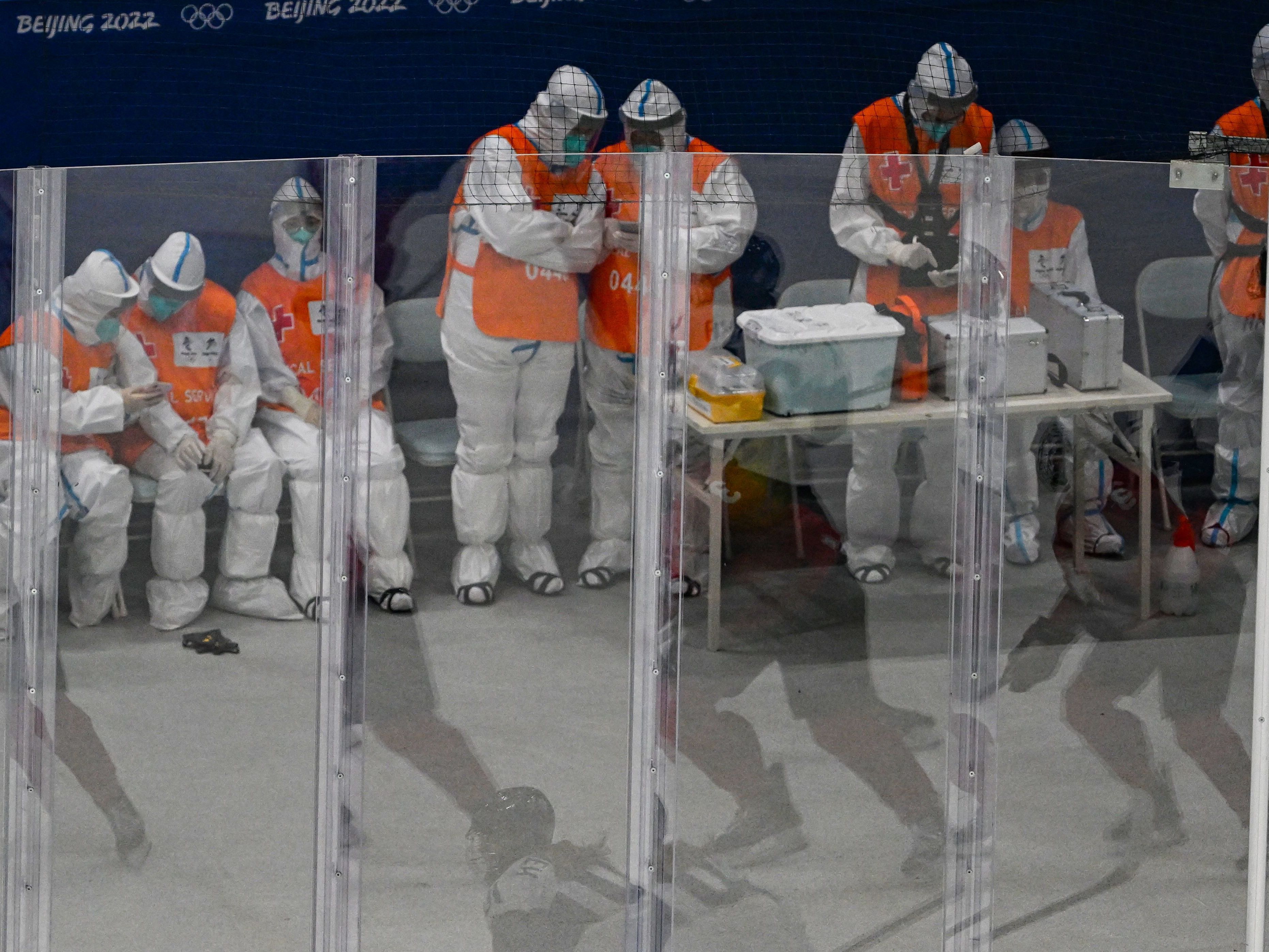 caption: Medical personnel wearing personal protective equipment keep watch during a hockey game at the Beijing 2022 Winter Olympic Games.