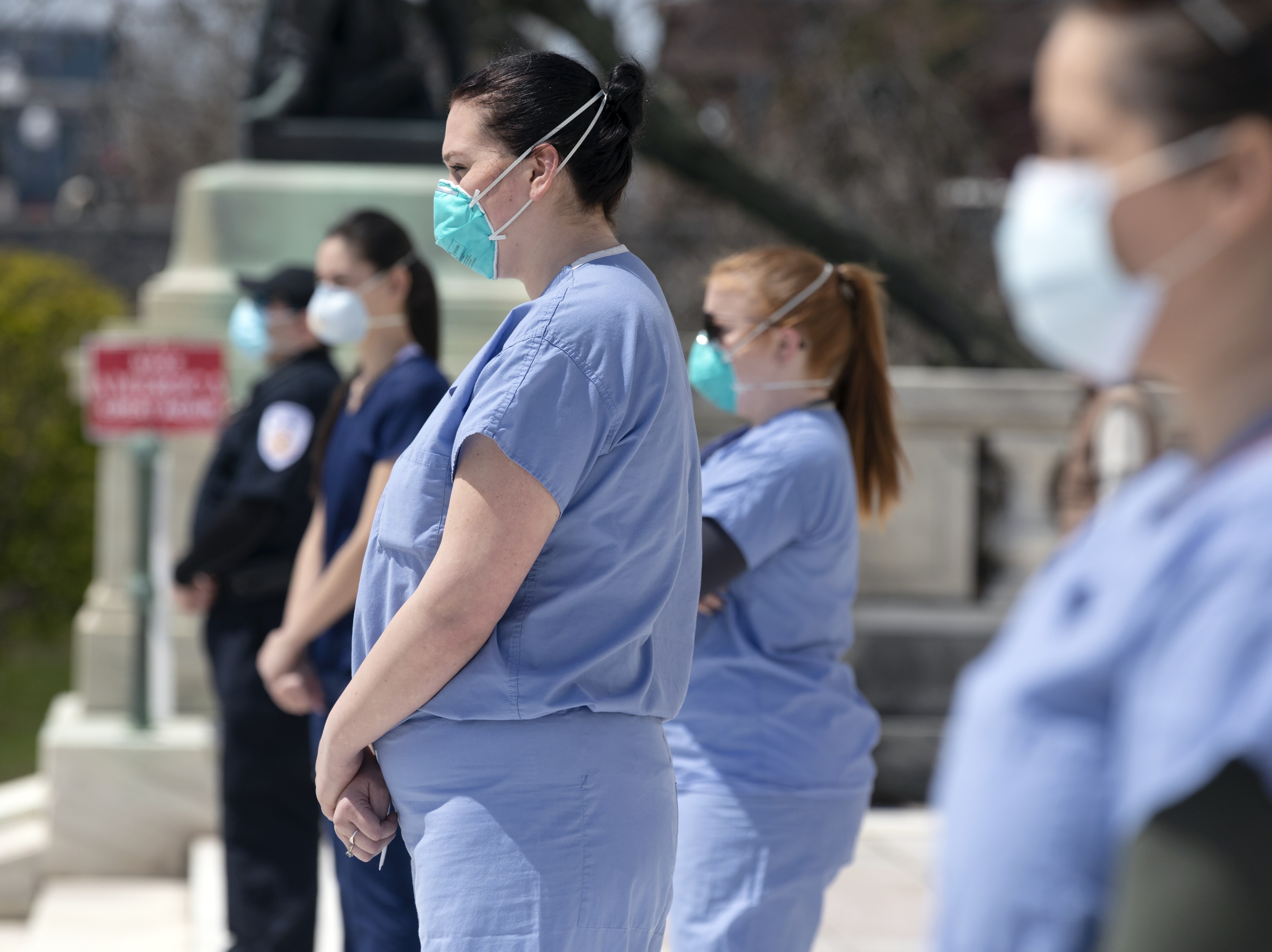 caption: Nurses stand in counter-protest during a demonstration against stay-at-home orders due to coronavirus concerns, at the State House in Providence, R.I., on Saturday.