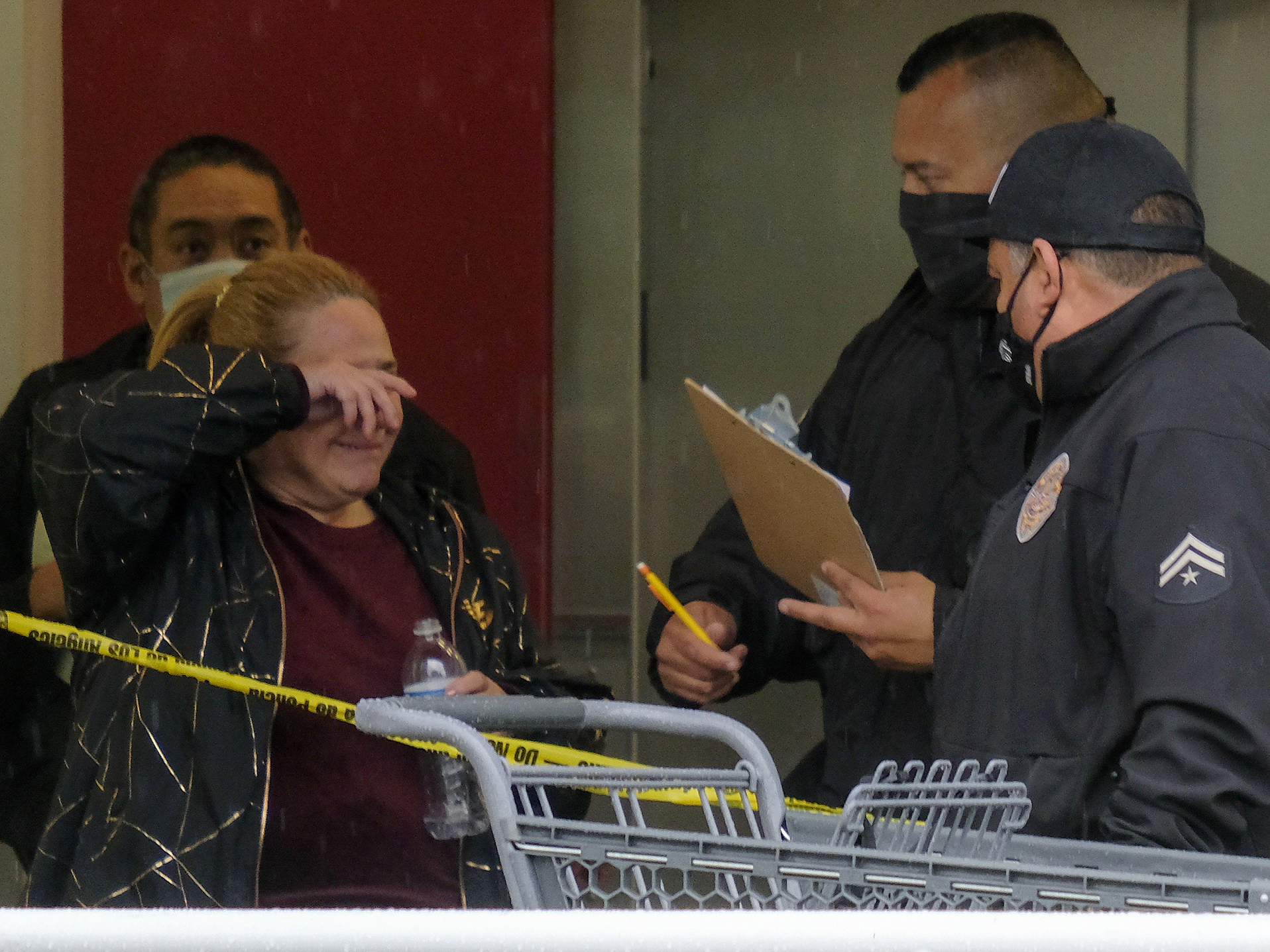 caption: A woman wipes her eye as police officers investigate the scene where two people were struck by gunfire in a shooting at a Burlington store as part of a chain formerly known as Burlington Coat Factory.