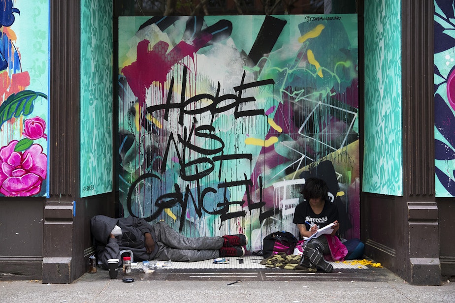 caption: Marty Jackson, left, and Gracie Ann, right, sit in the doorway of a boarded up business in front of a mural painted by artist Jay Michael that reads, 'Hope is Not Cancelled,' on Tuesday, April 28, 2020, along First Avenue South in Seattle. 