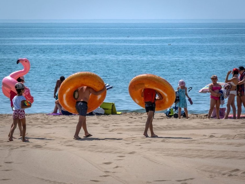 Children walk on the beach with rubber rings around their necks — and a pink flamingo — in Narbonne-Plage during a sunny day of summer on July 3, 2019.