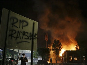 caption: "RIP Rayshard" is spray-painted on a sign as flames engulf a Wendy's restaurant during protests in Atlanta on Saturday over the death of Rayshard Brooks.