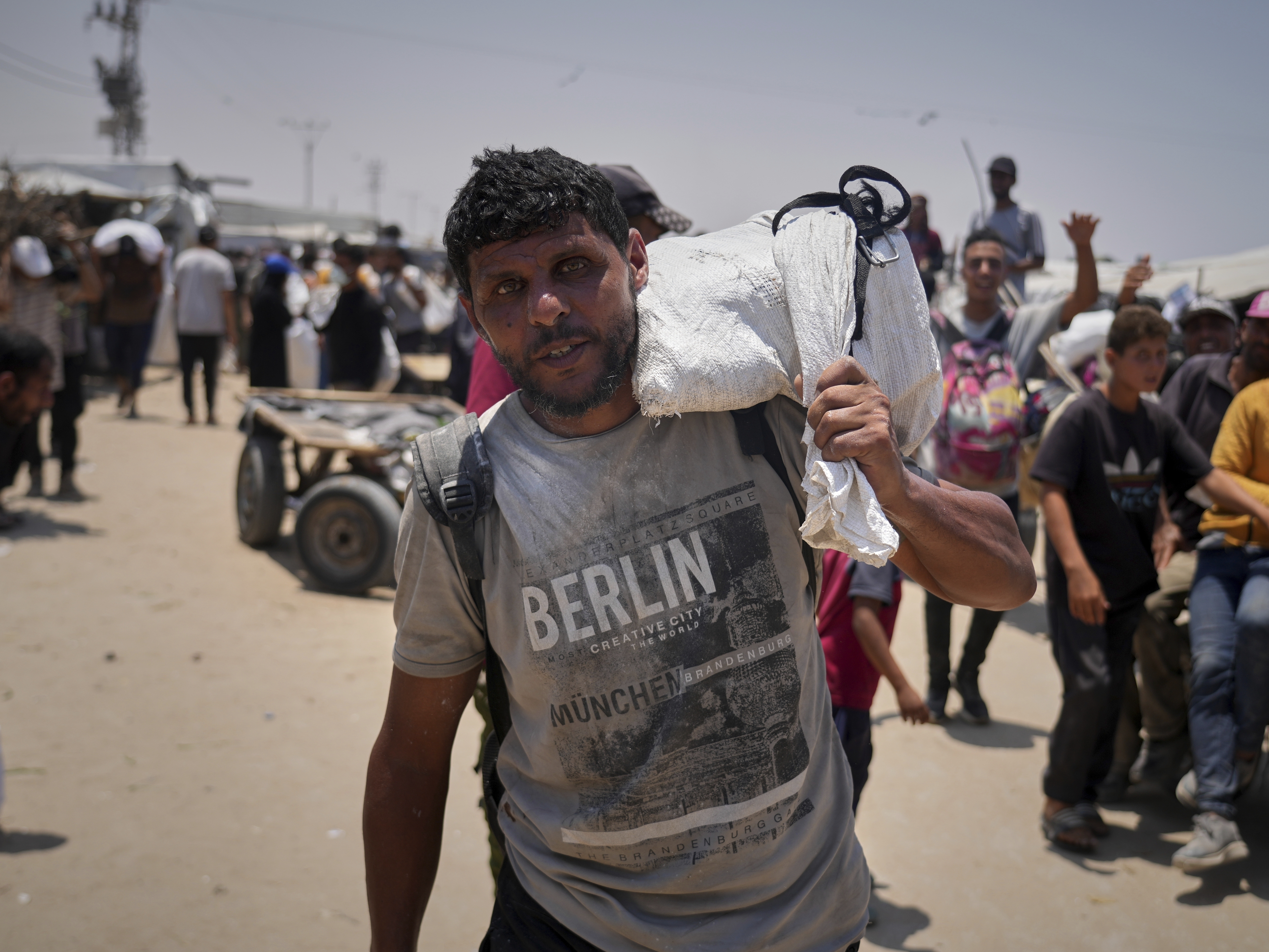 caption: Omar al-Hobi, 43, from Rafah, carries a bag of food he collected at a distribution center run by private contractor the Gaza Humanitarian Foundation in the southern Gaza Strip, as he arrives at his tent in Khan Younis, on June 10.