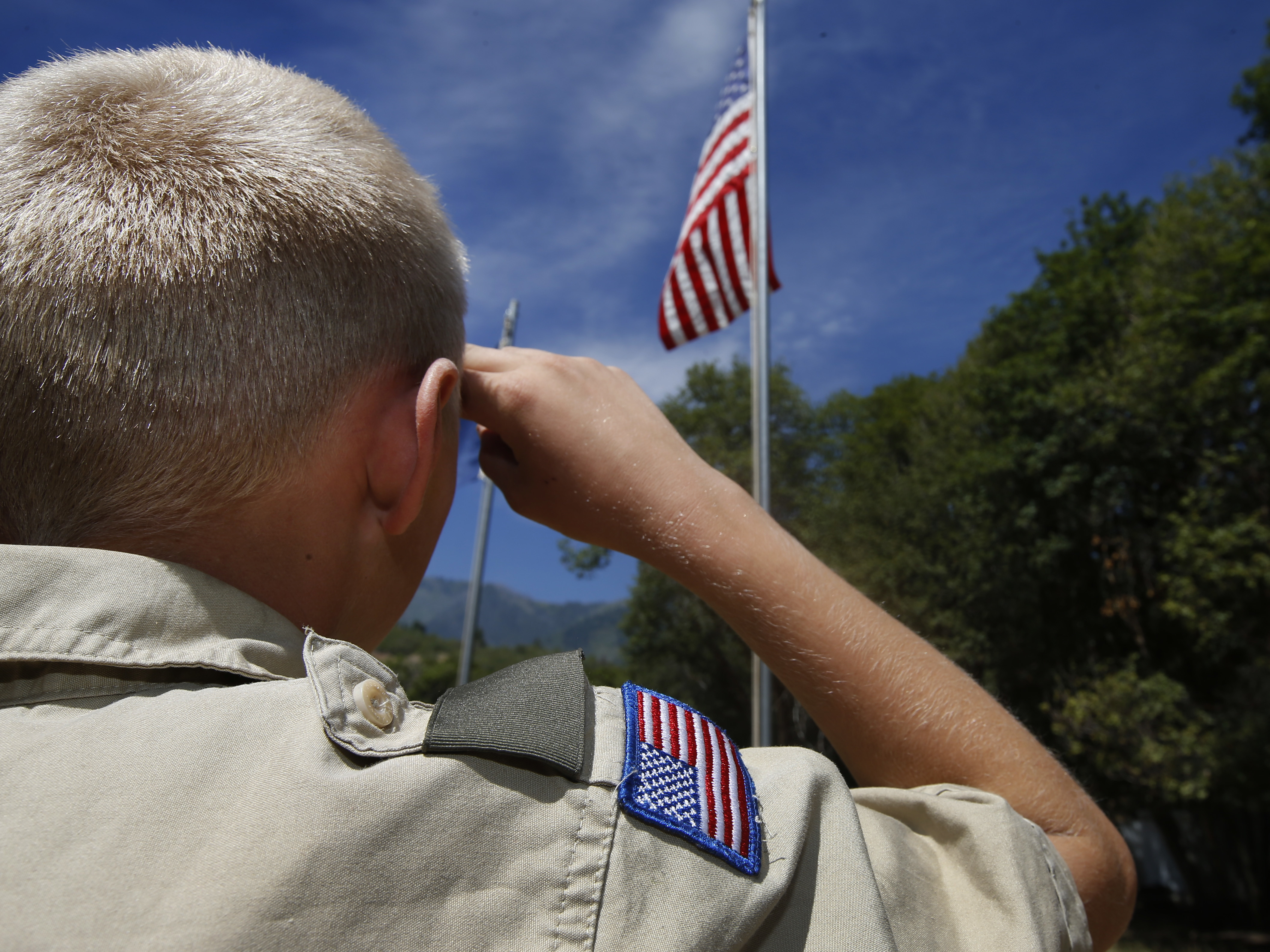 caption: A Boy Scout salutes the American flag at camp Maple Dell in 2015 outside Payson, Utah.