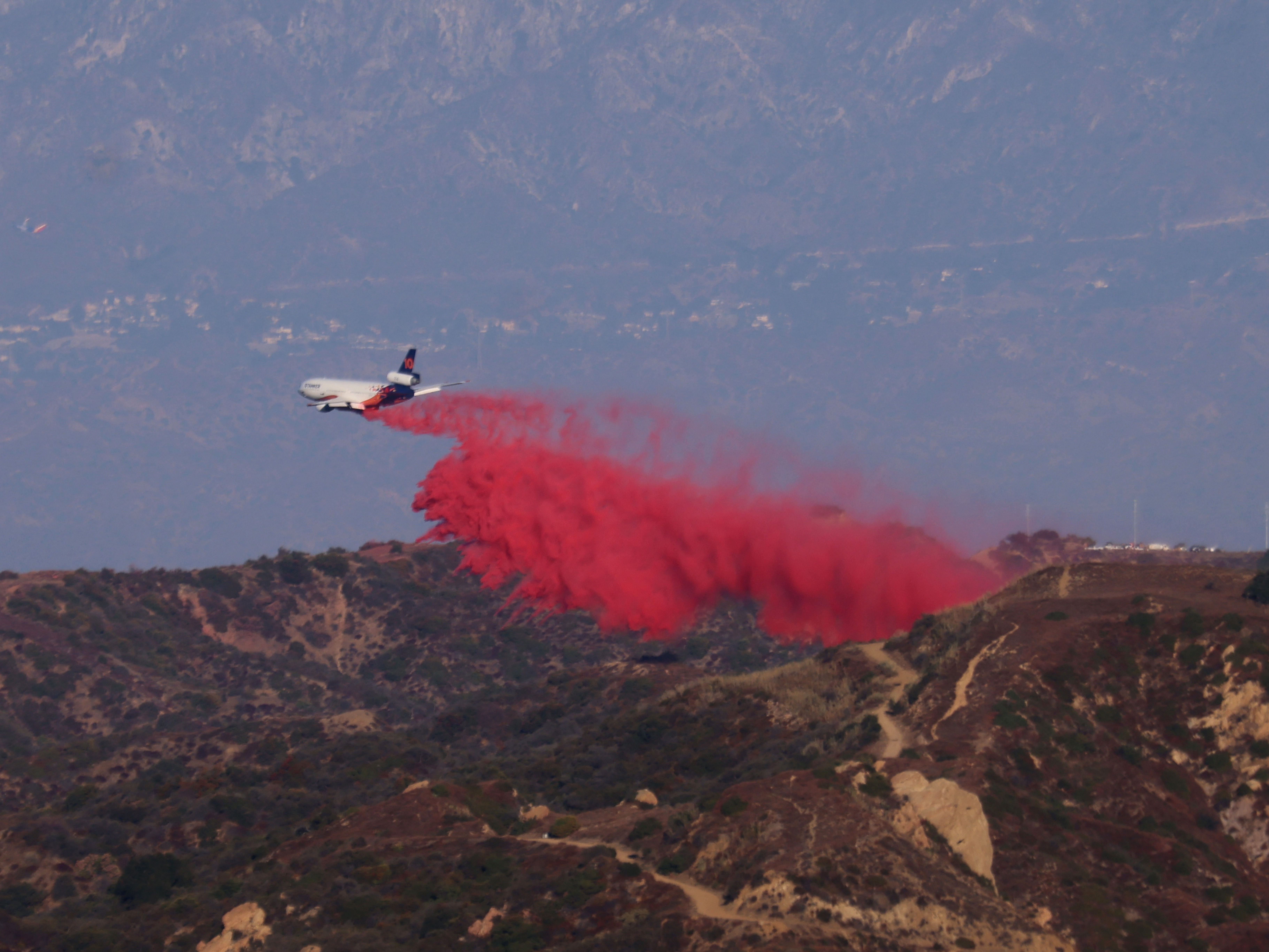 caption: A tanker drops retardant as the Palisades Fire grows in the mountains in Topanga, Calif., on Thursday