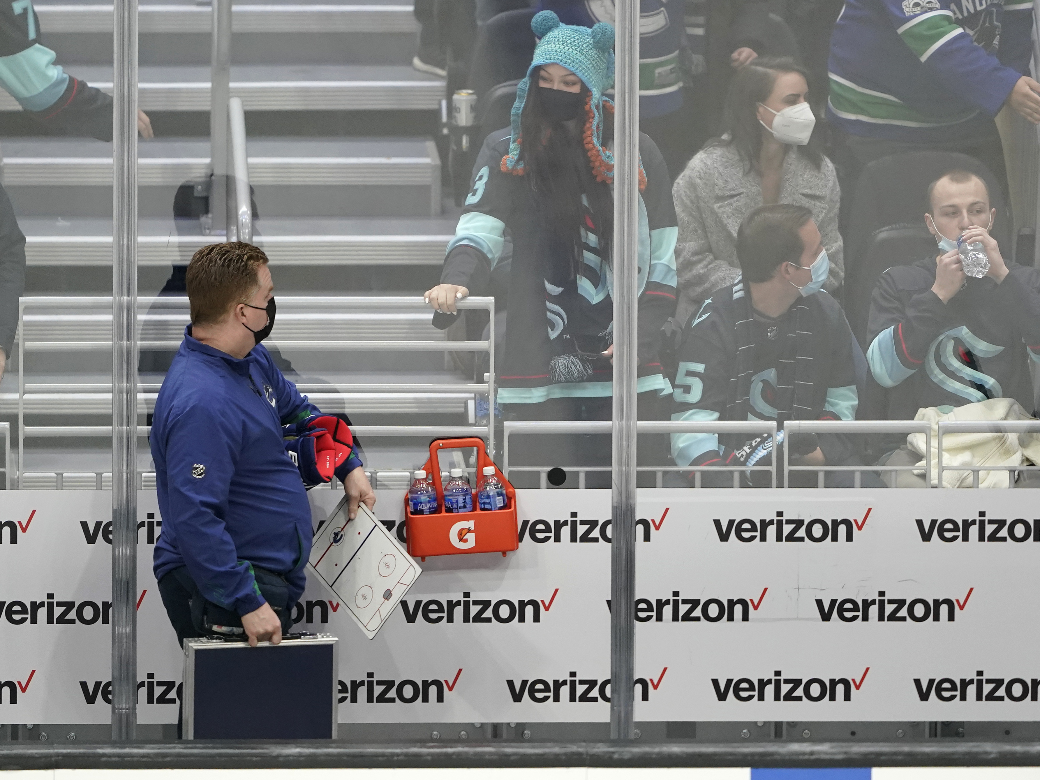 caption: Seattle Kraken fan Nadia Popovici, center, looks toward Vancouver Canucks assistant equipment manager Brian "Red" Hamilton, left, at the end of an NHL hockey game in Seattle on Saturday. Popovici had written Hamilton a note months earlier urging him to see a doctor about a suspicious mole, which turned out to be cancerous.
