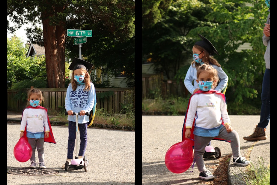 caption: Two neighborhood kids (Scarlett, with balloon, and Sipriana, wearing a graduation cap) watch the socially distanced graduation celebration on the block. Scarlett’s shirt says super, and she wears a cape.