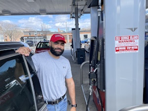 caption: Argenis Dominguez fueling up his SUV at a gas station in Boston. He drives Uber for a living and says the higher gas prices mean less money in his pocket.