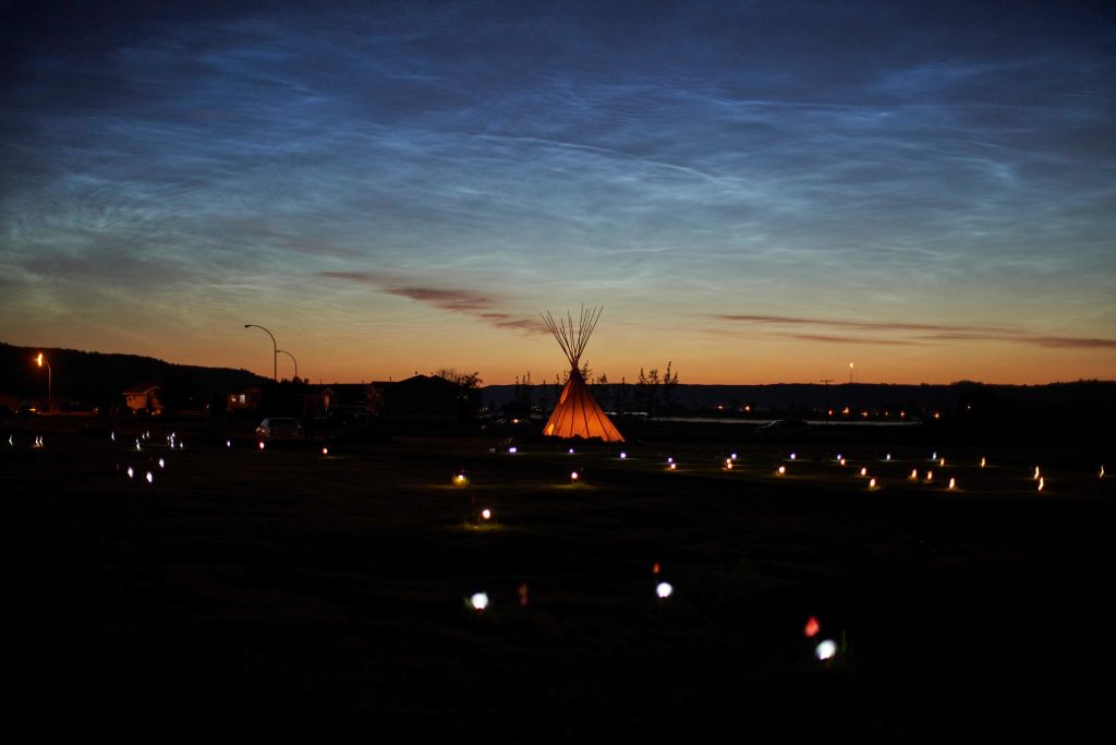 caption: Solar lights and flags mark the spots where 751 human remains were recently discovered in unmarked graves at the site of the former Marieval Indian Residential School on the Cowessess First Nation in Saskatchewan on June 27, 2021. (Geoff Robins/AFP/Getty Images)