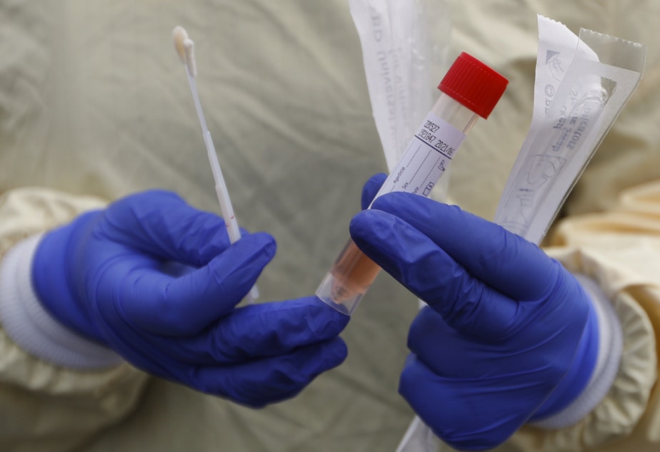 caption: A nurse holds swabs and a test tube to test people for COVID-19 at a drive through station set up in the parking lot of the Beaumont Hospital in Royal Oak, Mich.