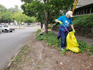 caption: Kathy Huntsman adds a bottle cap to her trash bag across the street from Gassworks Park. This is her fourth year cleaning up litter after the 4th of July fireworks show.
