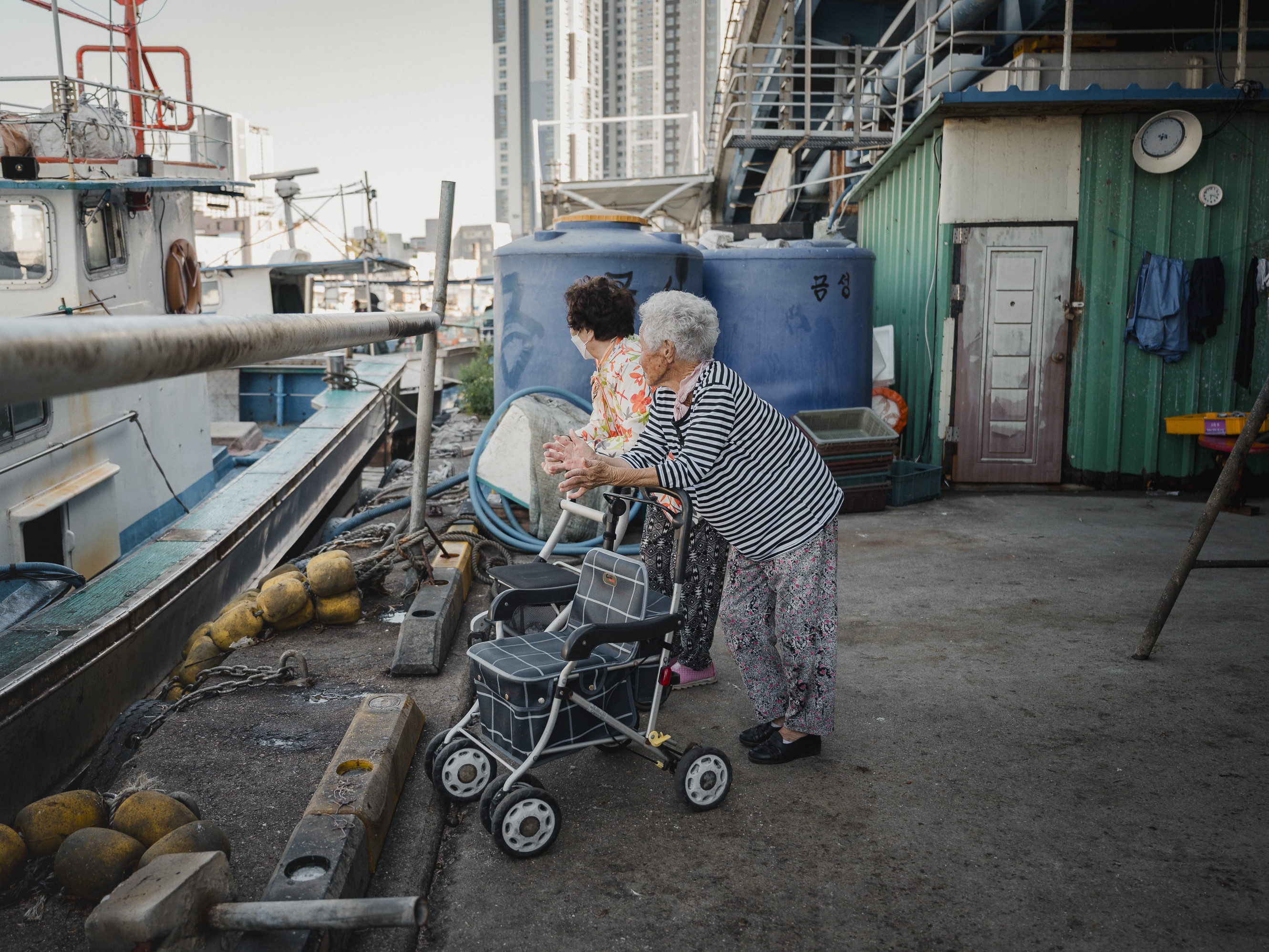 caption: Lee Choo-sum (left) and Lee Geum-soon look for free fish or seafood from boats in Abai Village on Sept. 8, 2023. Both women left North Korea when the war broke out and have lived in the village for the past 70 years.
