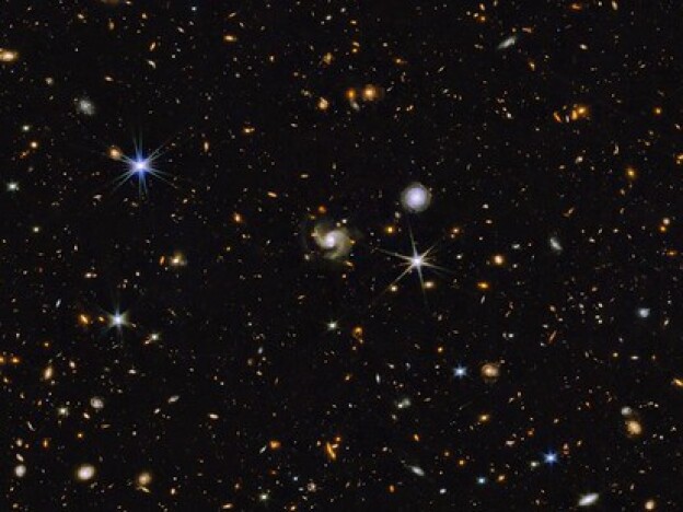 caption: This multi-wavelength image from NASA shows a universe full of galaxies that are various shapes, colors and sizes. Most are small while a handful are somewhat larger. A few stars are also scattered across the image.