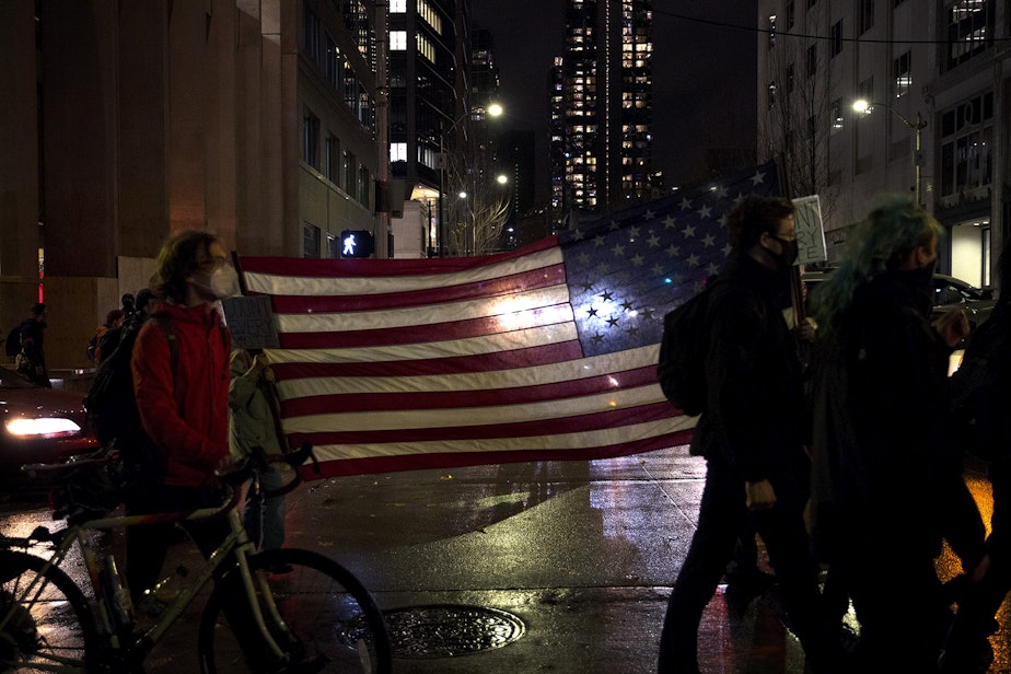 caption: Demonstrators carry an American flag as hundreds marched through Pioneer Square on Wednesday, November 4, 2020, in Seattle. The event was focused on counting every vote and protecting every person. In addition to supporting ongoing vote counts, speakers called for an investment in Black communities, closing King County's youth jail and protecting undocumented immigrants.