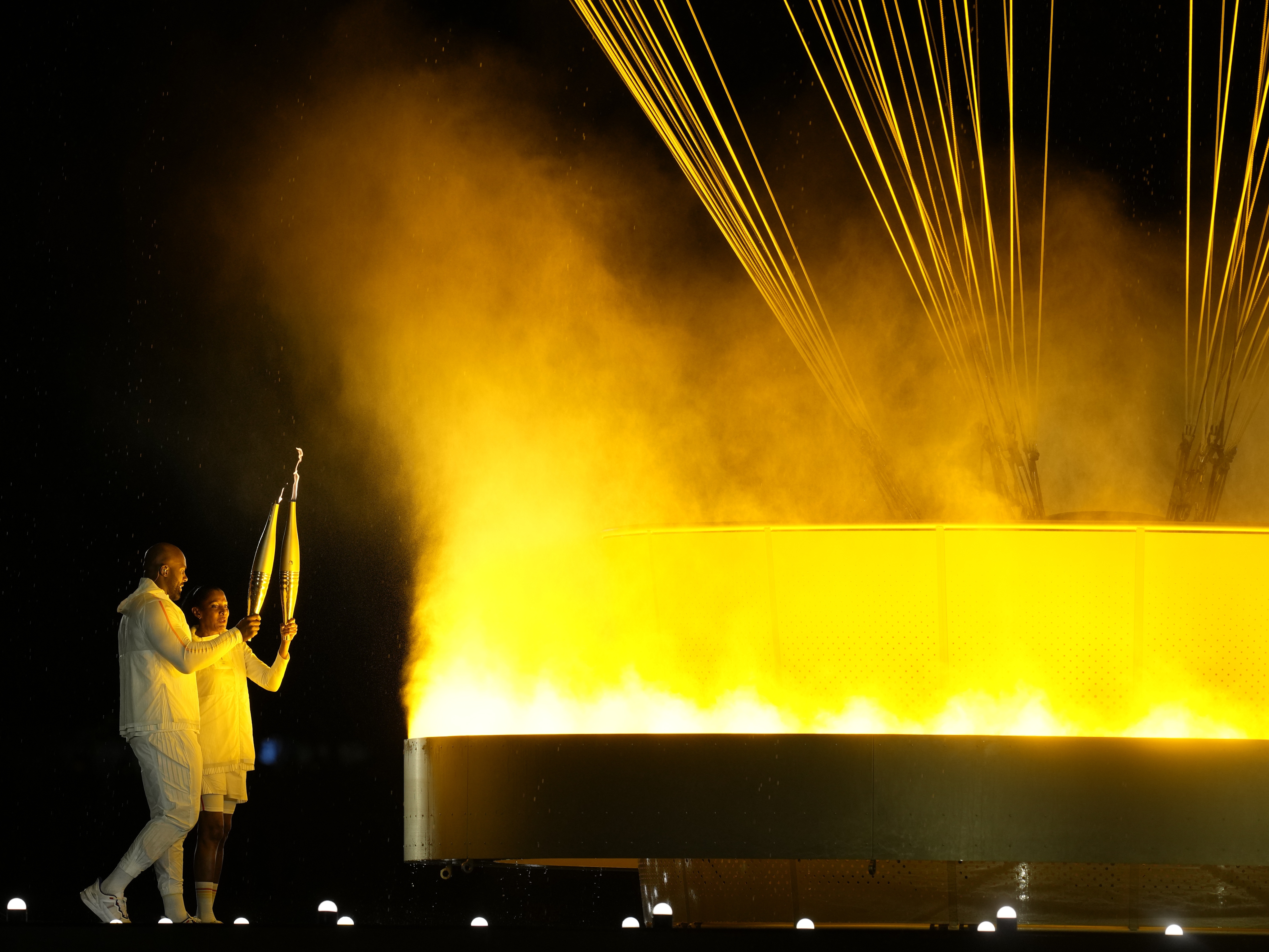 caption: The cauldron is lit by torch bearers Marie-Jose Perec and Teddy Riner in Paris, during the opening ceremony of the 2024 Summer Olympics, Friday, July 26, 2024.