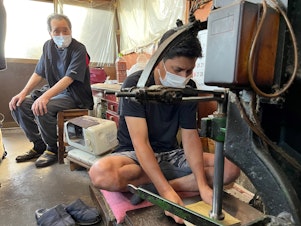 caption: Yoshikazu Netsuno (left) watches his son Shinichi hammer a thick stack of specialized paper. In between each sheet is a thin layer of gold leaf. "My son is going to take over this business, so in our case, we had a successor," Netsuno says. "Many other artisans' families in Kanazawa were not so lucky."