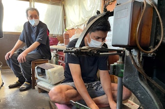 caption: Yoshikazu Netsuno (left) watches his son Shinichi hammer a thick stack of specialized paper. In between each sheet is a thin layer of gold leaf. "My son is going to take over this business, so in our case, we had a successor," Netsuno says. "Many other artisans' families in Kanazawa were not so lucky."
