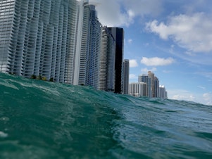 caption: Waves lap ashore near condo buildings in Sunny Isles, Fl., on Aug. 9, 2021. Rising sea levels are seen as one of the potential consequences of climate change and could impact areas such as Florida's Miami-Dade County.