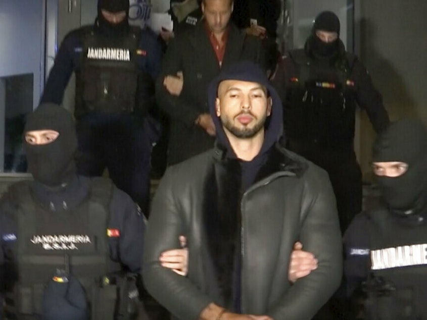 caption: In this grab taken from video released by Observator Antena 1, Social Media personality Andrew Tate is led away Thursday by police, in the Ilfov area, north of Bucharest, Romania.