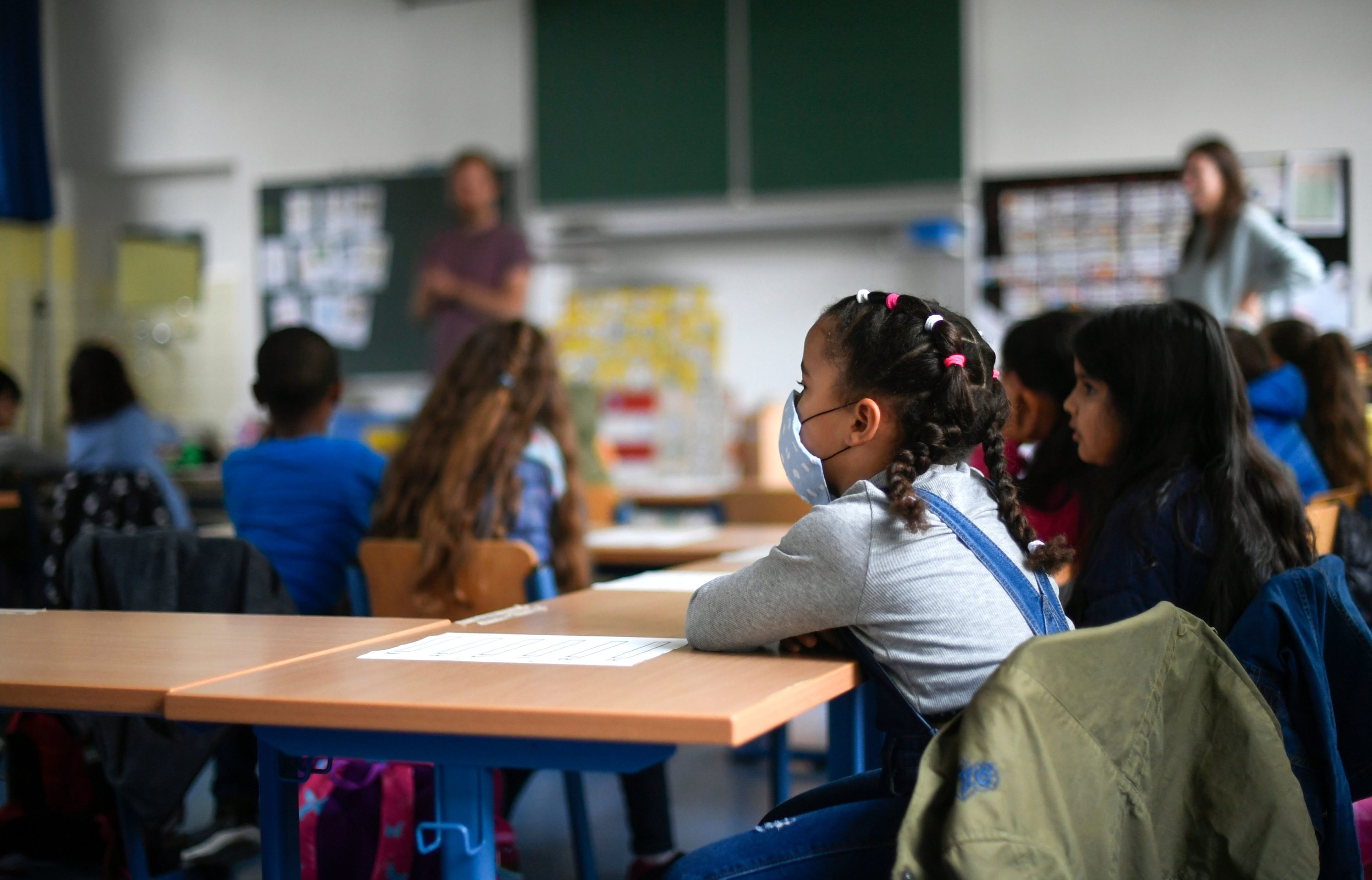 caption: A girl wears a face mask as students sit in a classroom in Germany. (INA FASSBENDER/AFP via Getty Images)