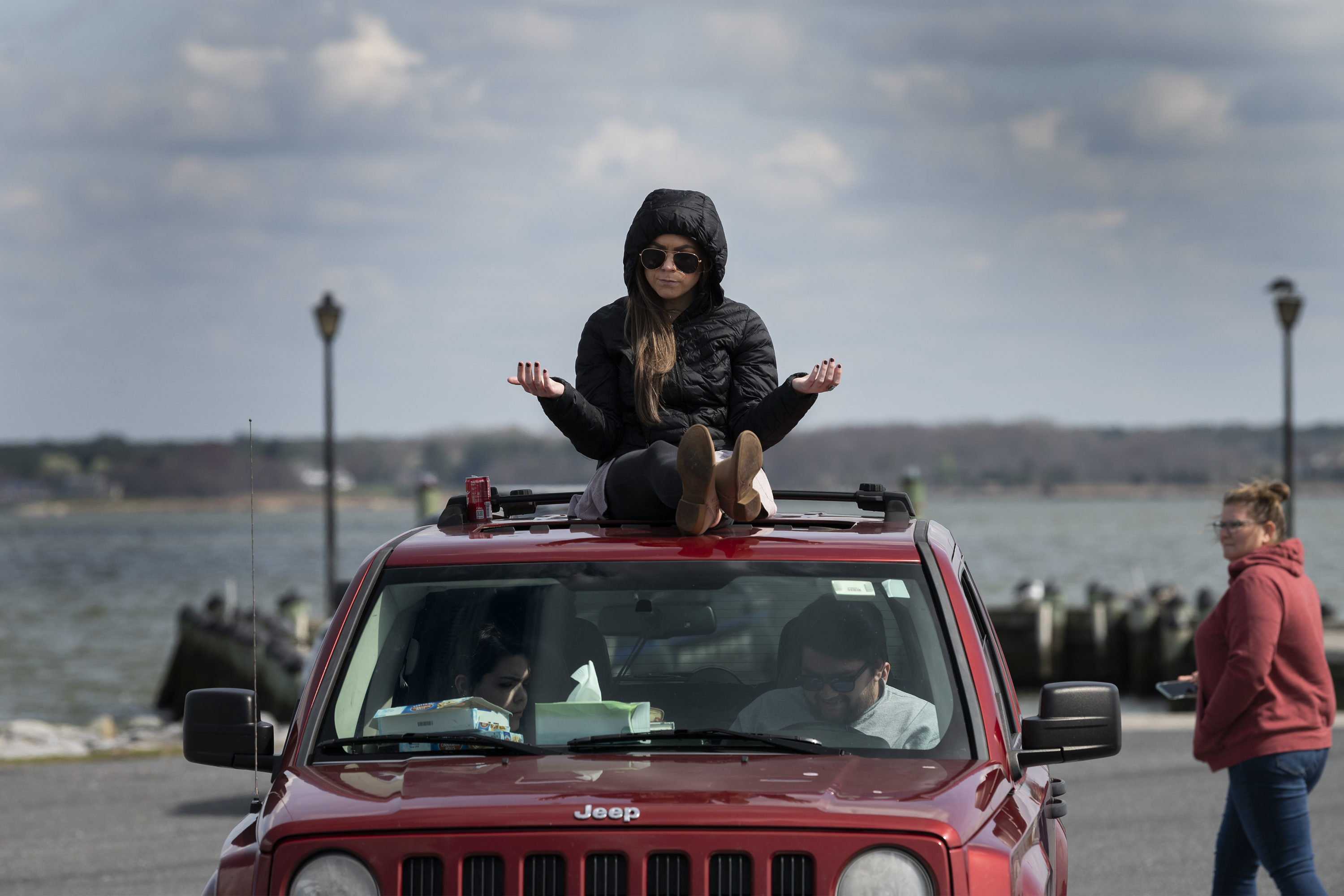 caption: A member of Jesus' Church prays on top of a car during a Sunday church service held at Great Marsh Park in Cambridge, Maryland, on March 22, 2020. (JIM WATSON/AFP via Getty Images)