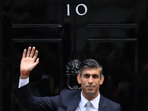 caption: Rishi Sunak waves outside to door to No. 10 Downing Street on Tuesday after delivering his first speech as prime minister.