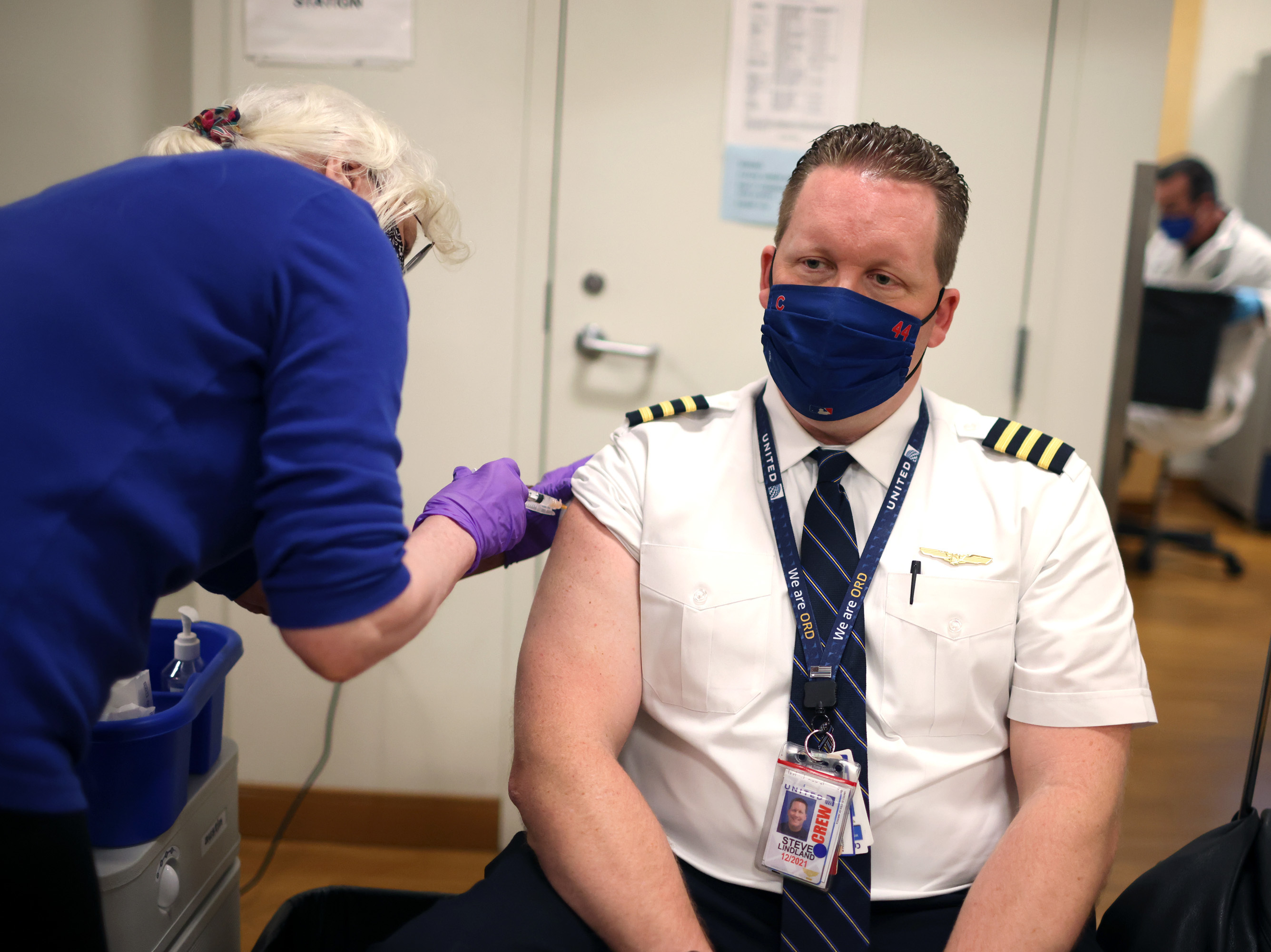 caption: United Airlines pilot Steve Lindland receives a COVID-19 vaccine at O'Hare International Airport.