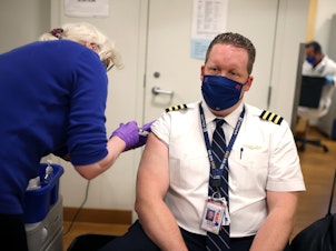 caption: United Airlines pilot Steve Lindland receives a COVID-19 vaccine at O'Hare International Airport.