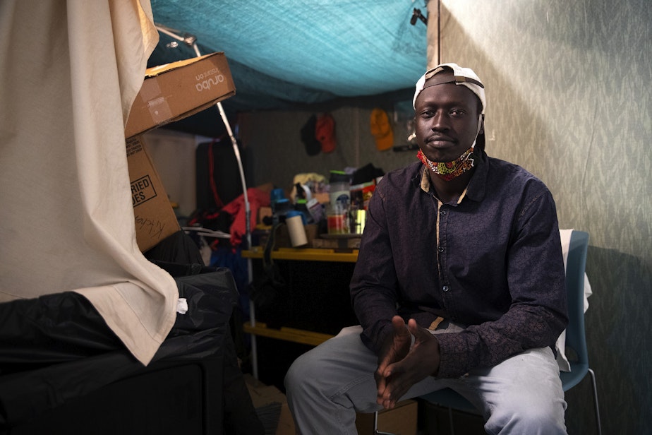 caption: Khames, 28, is portrayed in his portion of a residential dorm room at the Bridge shelter along Elliott Avenue on Monday, July 17, 2023, in Seattle. 