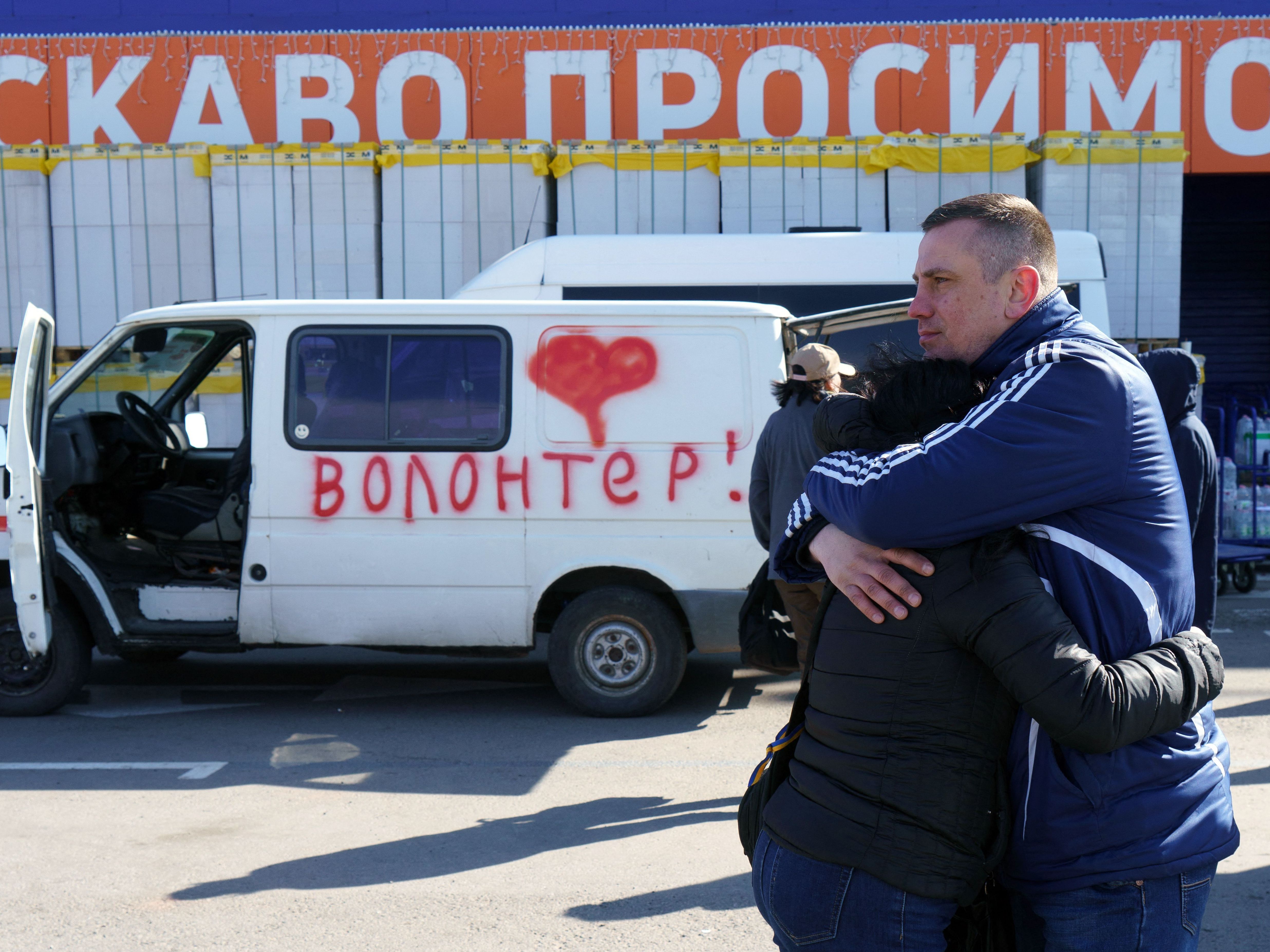 caption: Olga and Oleksandr hug as they wait beside a vehicle painted with the word "volunteers" at an evacuation center in Zaporizhzhya, Ukraine, on Tuesday. Olga's father is stuck in Mariupol, and Oleksandr is hoping to get in a volunteer convoy to the city, now under Russian siege.