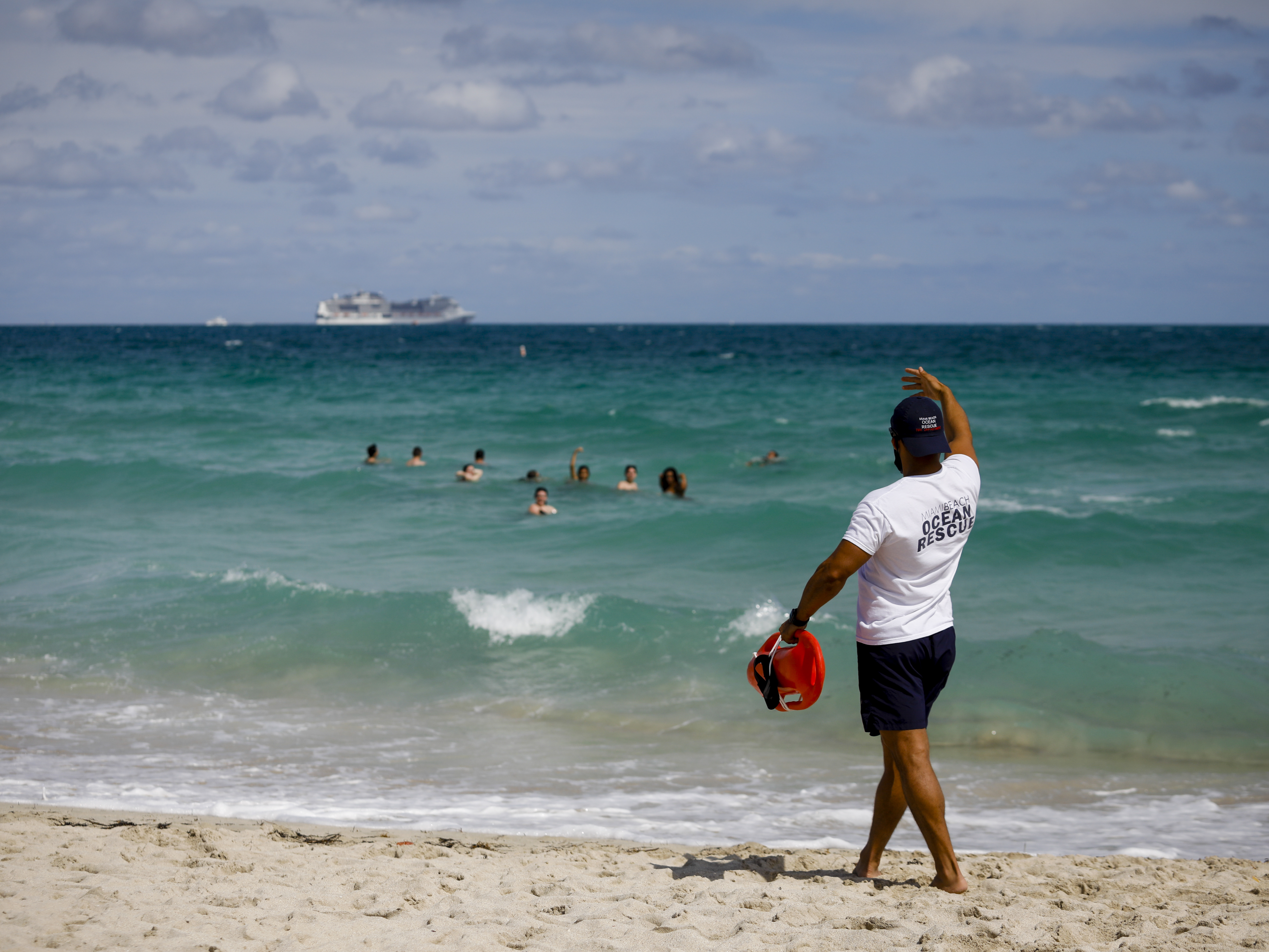caption: A lifeguard calls to swimmers at a beach in Miami on March 5. Amid fears of crowds fueling a new surge in coronavirus cases, Miami Beach on Saturday announced an abrupt curfew to curb swelling crowds of spring breaker visitors.